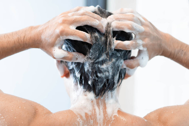 Gros plan jeune homme laver les cheveux avec shampooing dans la salle de bain, concept de soins de santé, accent sélectif
 - Photo, image