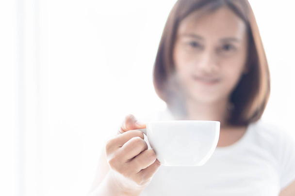 窓からの光の上にホットコーヒーのカップを保持しているクローズアップ女性,選択的な焦点 - 写真・画像