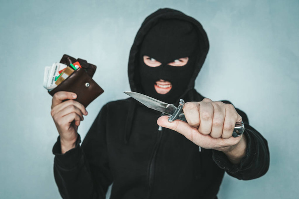 criminal robbery concept. An evil robber threatens with a knife and holds a stolen purse in his hand. Mortal danger. malevolent thief smiles. - Foto, immagini