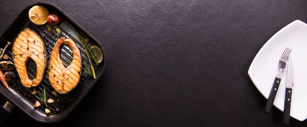 Grillezett lazac hal, különböző zöldségek serpenyőben fekete kő háttér - Fotó, kép