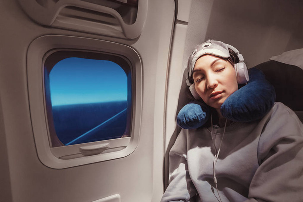 Ασιατικό κορίτσι κοιμάται στη θέση της στο αεροπλάνο κοντά στο παράθυρο στο  - Φωτογραφία, εικόνα