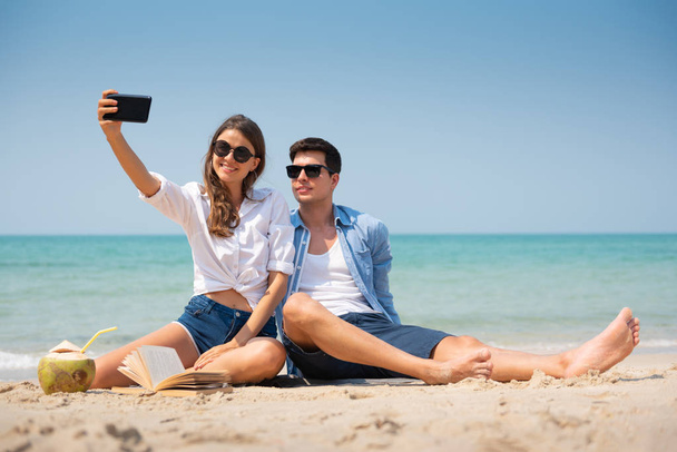 Улыбающаяся молодая пара делает селфи на пляже
. - Фото, изображение
