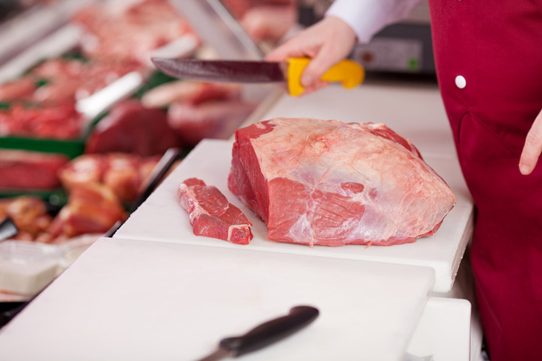saleswoman cutting meat on board at counter - Photo, Image