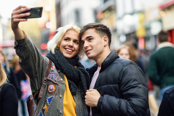 Feliz pareja de turistas tomando selfie en una calle llena de gente
. - Foto, Imagen