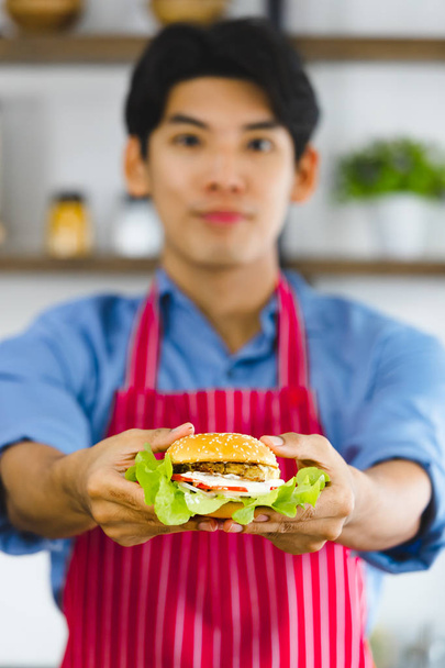 Asyalı adam elinde hamburgeri tutuyor. - Fotoğraf, Görsel