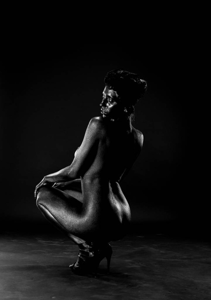 Naked woman painted in black on a white background in the studio. - Photo, Image