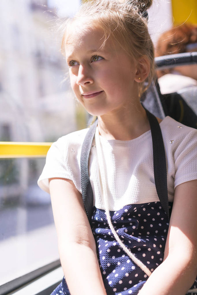 Pikkutyttö menee bussilla. Koulutyttö istuu koulubussissa ja valmis hänen ensimmäinen ratsastaa. pystyvalokuva
 - Valokuva, kuva