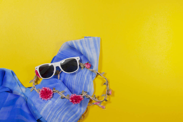 Белые солнцезащитные очки, красные цветы и синий шарф на желтой поверхности
 - Фото, изображение