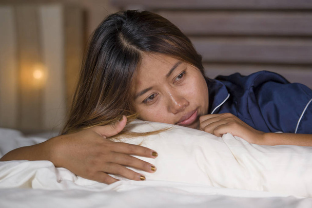 dramatyczny styl życia młody atrakcyjny smutny i przygnębiony Asian kobieta w piżamie leżącego w łóżku w bólu cierpienia depresji i lęku uczucie samotności i zdesperowany - Zdjęcie, obraz