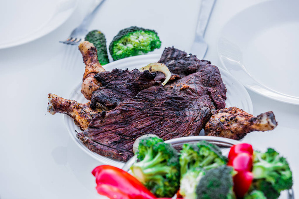 Gegrilltes Rindfleisch und Hühnchen mit Gemüse auf einem Tisch. Seitenansicht - Foto, Bild
