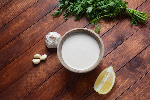 Tahini sauce made from sesame seeds in bowl with parsley on wooden background - Photo, Image