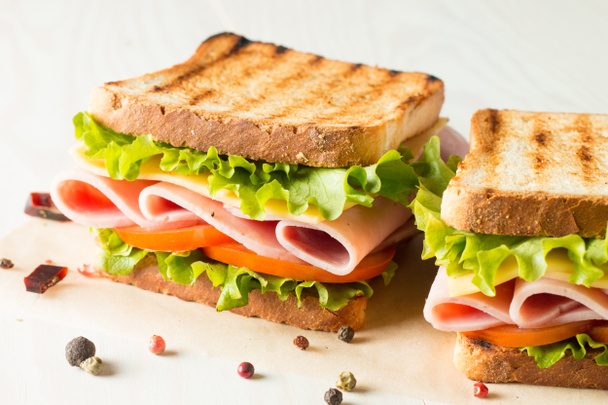 Close-up photo of a club sandwich. Sandwich with meat, prosciutto, salami, salad, vegetables, lettuce, tomato, onion and mustard on a fresh sliced rye bread on wooden background. Olives background. - Photo, Image