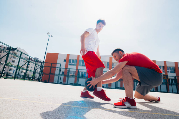 赤いスポーツのエキュアップメントを着た2人の白人の友人がバスケットを演奏 - 写真・画像