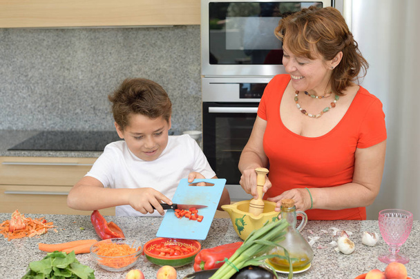 Matka i syn przygotowują obiad i uśmiechy. Syn tnie czerwona papryka - Zdjęcie, obraz