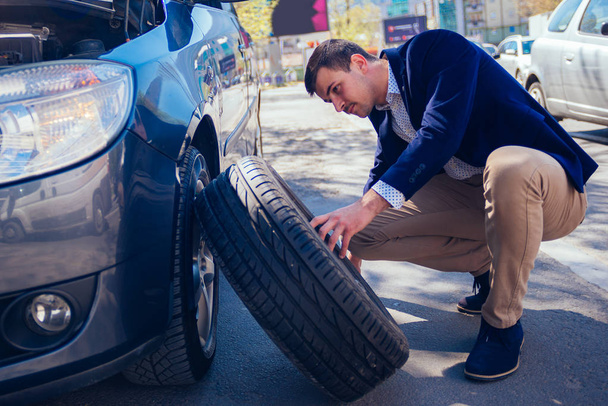 A tired businessman on a sunny day is taking a tire out of his c - Valokuva, kuva