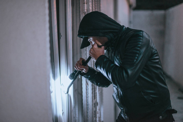 Hombre encapuchado con linterna que entra en casa
 - Foto, Imagen