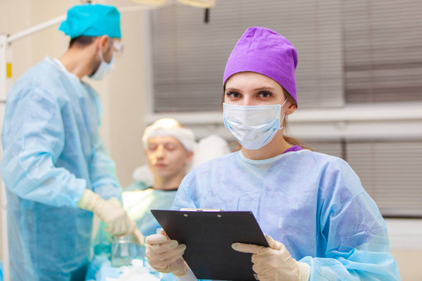 Beautiful portrait of a doctor with documents on the background of the operating room. Baldness treatment. Hair transplant. Surgeons in the operating room carry out hair transplant surgery. Surgical - Photo, image