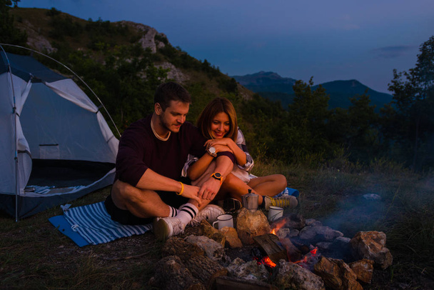 Jeune couple se détendre au coin du feu de camp et boire du café dans le
 - Photo, image