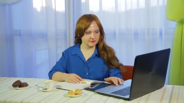 Uma mulher de cabelos castanhos em um café em uma mesa trabalha com um laptop e bebe café
 - Filmagem, Vídeo