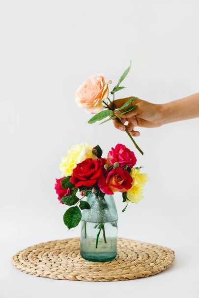 samenstelling van kleurrijke rozen in een vaas op een rieten servet op een witte achtergrond - Foto, afbeelding