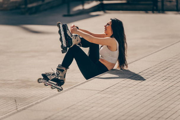 Girl sitting on wall and puts on skates - Фото, изображение