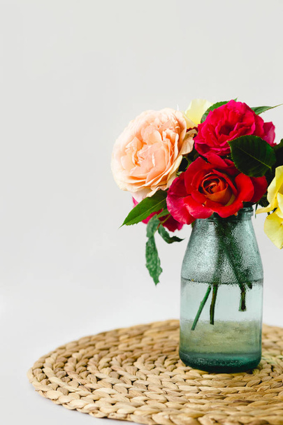 Coloful roses in vase on a wicker napkin on white background - Photo, Image