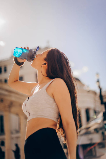 Здоровая и спортивная молодая женщина пьет воду из бутылки
 - Фото, изображение