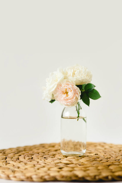 Красиві троянди в скляній вазі на плетеній серветці на білому тлі
 - Фото, зображення