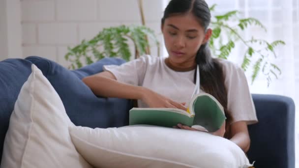 Asian woman reading book and cell phone on sofa in living room at home. - Filmagem, Vídeo
