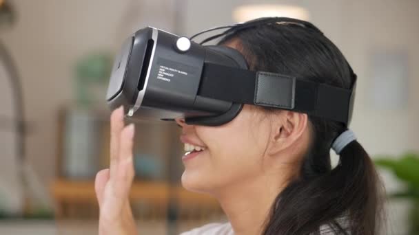 Portrait of young asian woman using a virtual reality headset in living room at home. Smile happy girl getting experience using VR. - Footage, Video