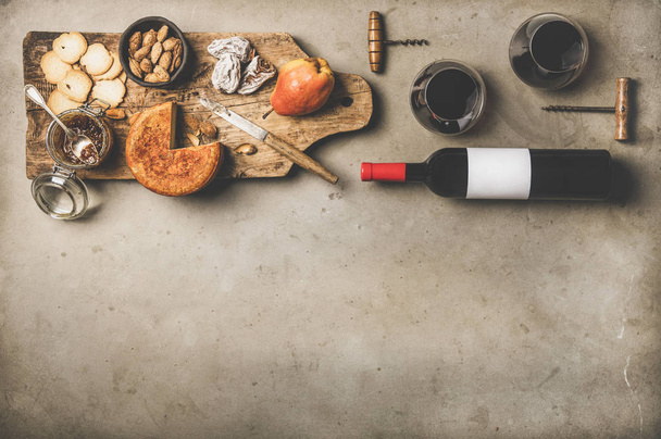 Wine and snack set. Flat-lay of wine bottle with blank label, vintage corkscrews, glasses with wine, cheese and appetizers on board over concrete background, top view, copy space. Party food concept - Fotoğraf, Görsel