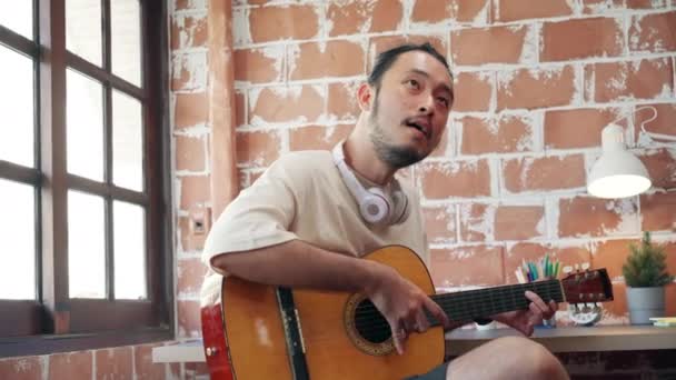 Виконавці створюють музику в домашній звуковій студії, азійський чоловік грає на гітарі і співає вдома у вітальні. Вранішнє життя чоловіка розслаблює вдома.. - Кадри, відео
