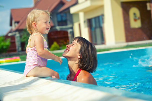 Summer vacation. Pretty baby girl with her mother in swimming pool outdoors - Zdjęcie, obraz