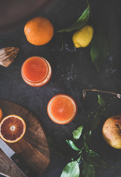 Flat-lay of two glasses of freshly squeezed blood orange juice or smoothie and fresh fruits on dark background, top view. Healthy lifestyle, vegan, vegetarian, alkaline diet, spring detox concept - Fotoğraf, Görsel