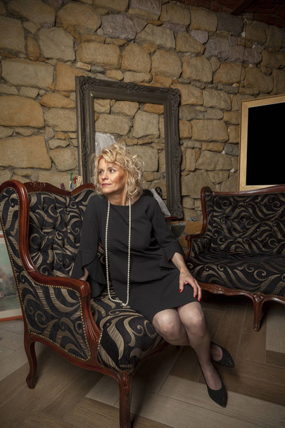 middle aged woman in black dress sitting on sofa - Foto, Bild
