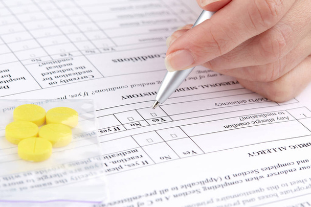 Gele pillen en hand schrijven op medische vragenlijst formulier - Foto, afbeelding
