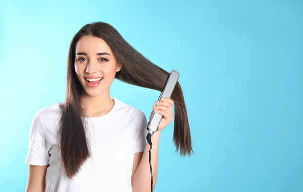 Happy woman using hair iron on color background. Space for text - Фото, зображення