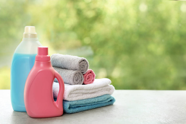 Stack of clean towels with detergents on table against blurred background. Space for text - Φωτογραφία, εικόνα