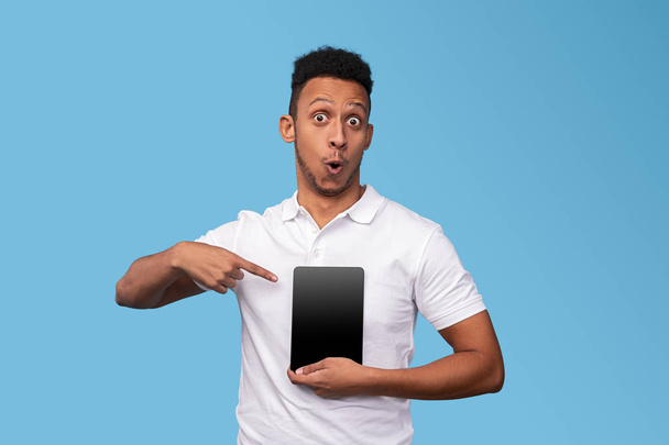 Удивленный черный мужчина указывает на планшет с пустым экраном
 - Фото, изображение
