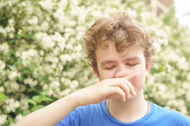 Teenager mit Allergien steht in blauem T-Shirt zwischen Jasminsträuchern und leidet an schlechter Gesundheit - Foto, Bild