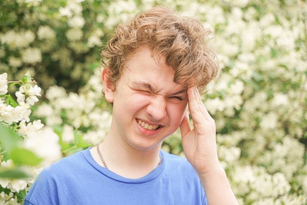 Adolescente con alergias de pie en una camiseta azul entre los arbustos de jazmín y sufre de mala salud
 - Foto, imagen