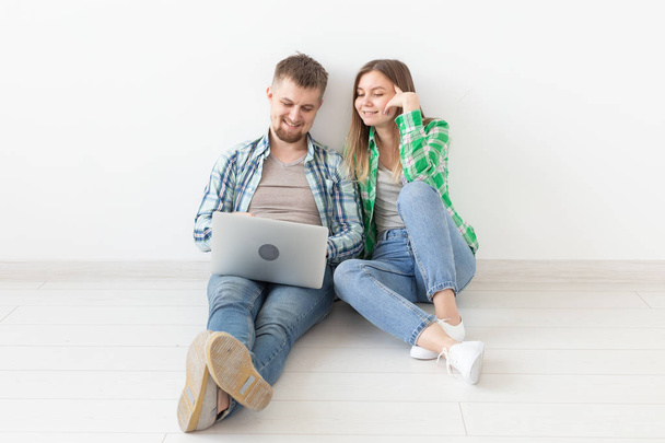 Glimlachend jong paar maakt online aankopen van meubilair in hun nieuwe hypotheek appartement. Online Shopping concept met laptop - Foto, afbeelding