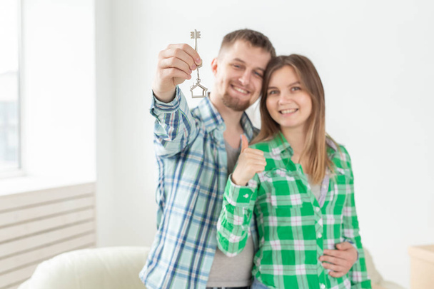Joven positivo cJoven pareja positiva sosteniendo las llaves de un nuevo apartamento mientras está de pie en su sala de estar
. - Foto, Imagen
