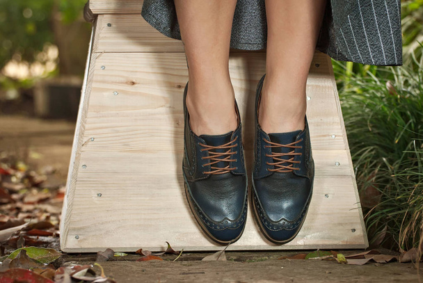 Γυναικείες δερμάτινες μπότες από κοντά. Το κορίτσι περπατά σε παπούτσια με φόντο ενορεία με τροπικά φυτά. Παπούτσια στυλ Οξφόρδης. - Φωτογραφία, εικόνα