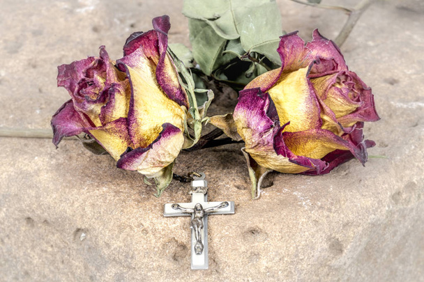 Cruz cristiana en rosario y rosas rojas amarillas secas yacen sobre una piedra arenisca
 - Foto, Imagen