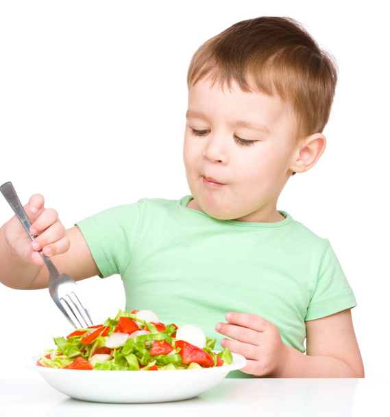 Cute little boy is eating vegetable salad - Foto, afbeelding