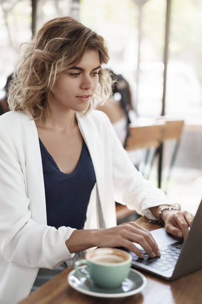 Vertical shot attractive successful businesswoman stylish white jacket sit cafe co-working space drink coffee cappucino look laptop display typing contact customer, writing reports, prepare project - 写真・画像
