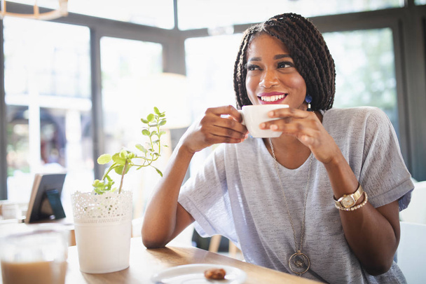 Beautiful young african woman enjoying a cup of coffee while relaxing at rastaurant - Photo, Image