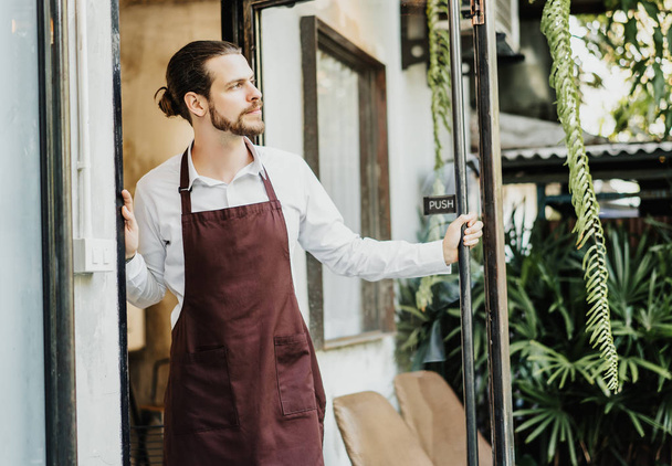 Knappe jonge man in schort werken serveerster in Café opening ent - Foto, afbeelding
