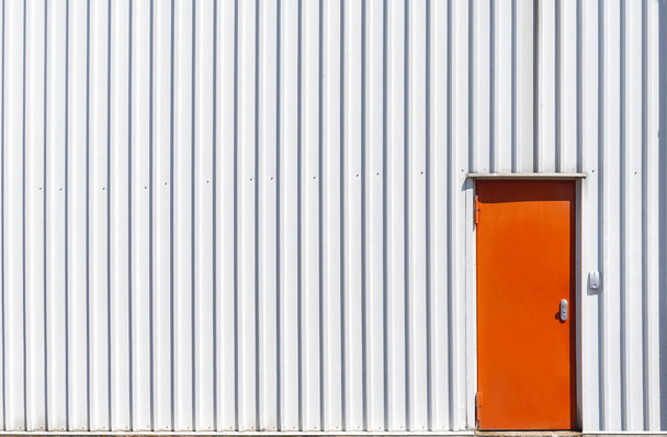 Puerta de metal naranja y una pared de almacén blanca
 - Foto, Imagen
